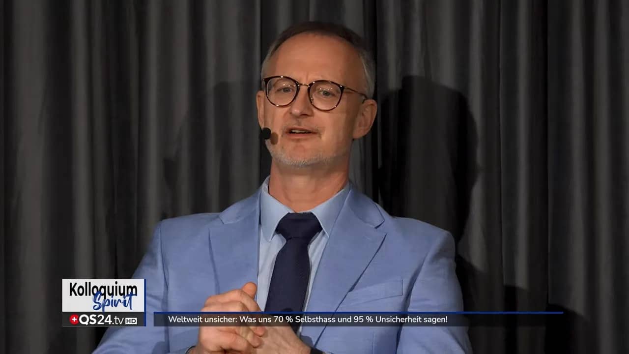 Weltweit unsicher: Was uns 70 % Selbsthass und 95 % Unsicherheit sagen! 5 Moderator in hellblauem Anzug spricht frontal vor dunklem Vorhang