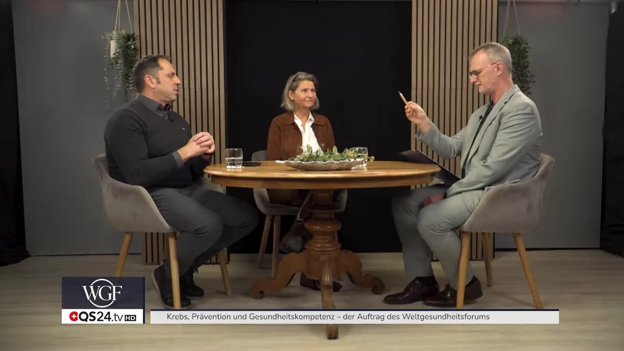 Moderator im grauen Sakko spricht und gestikuliert im Studio