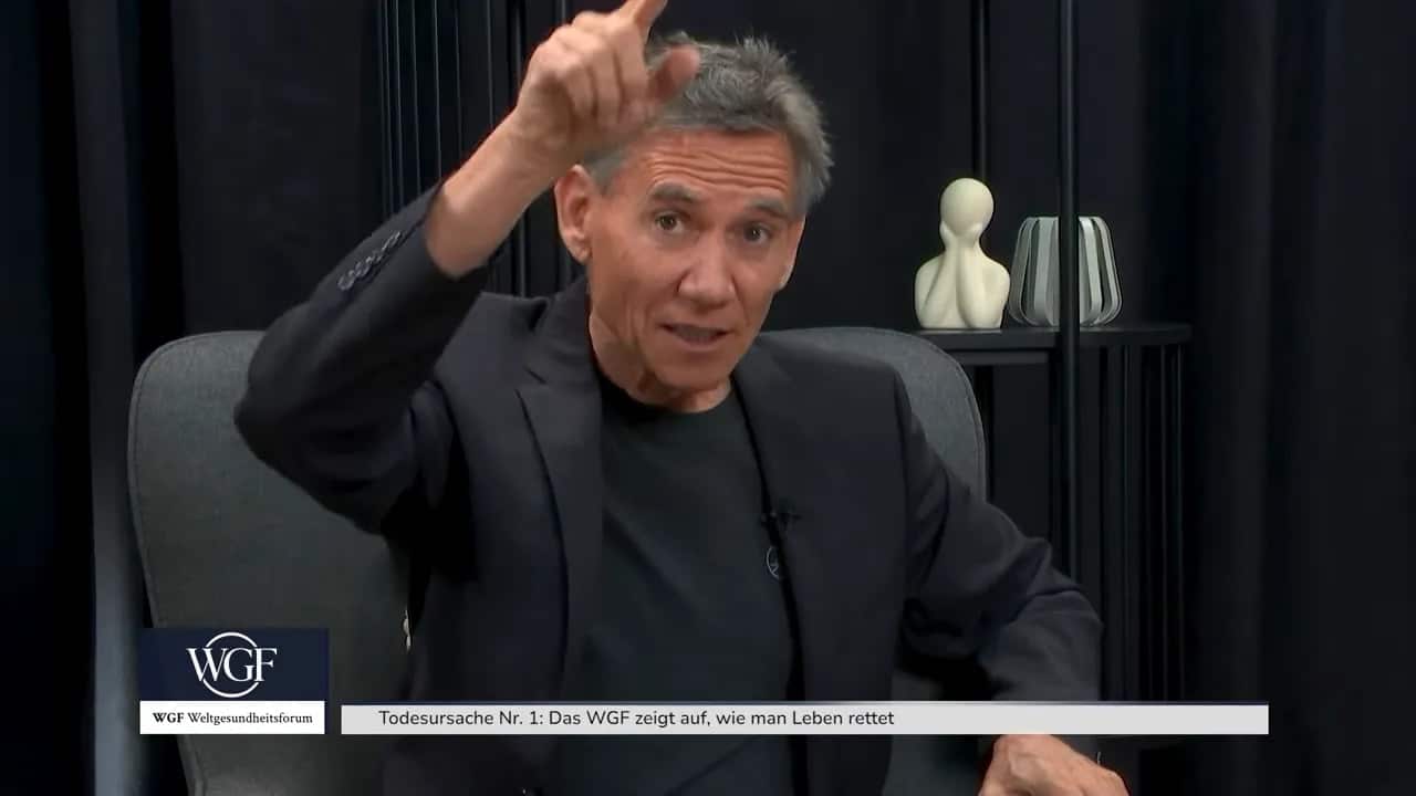 Kurt Mosetter sitzt im Sessel und zeigt mit beiden Händen eine waagerechte Linie