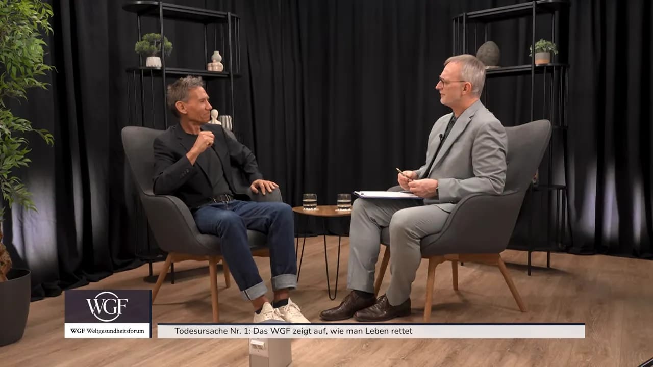 Kurt Mosetter sitzt im Sessel und zeigt mit beiden Händen eine waagerechte Linie